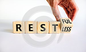 Restless or restful symbol. Businessman turns the wooden cube, changes the word `restless` to `restful`. Beautiful white table