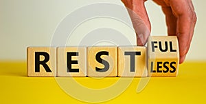 Restless or restful symbol. Businessman turns the wooden cube, changes the word `restless` to `restful`. Beautiful yellow tabl