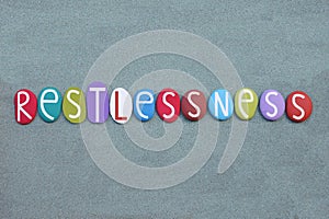 Restlessness, the inability to rest or relax, creative text composed with multi colored stone letters ovwer green sand photo