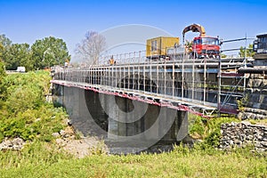 Restoration of an old damaged concrete bridge crossing a river with truck working