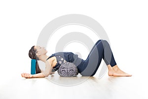 Restorative yoga with a bolster. Young sporty attractive woman in bright white yoga studio, lying on bolster cushion photo