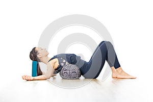 Restorative yoga with a bolster. Young sporty attractive woman in bright white yoga studio, lying on bolster cushion