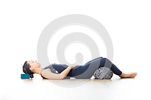 Restorative yoga with a bolster. Young sporty attractive woman in bright white yoga studio, lying on bolster cushion