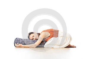 Restorative yoga with a bolster. Young sporty attractive woman in bright white yoga studio, lying on bolster cushion photo