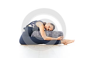 Restorative yoga with a bolster. Young sporty attractive woman in bright white yoga studio, lying on bolster cushion photo