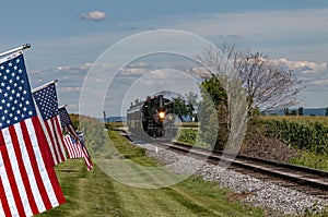 Restored Antique Steam Passenger Train Approaches a Fence With Gently Waving American Flags on It