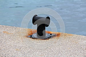 Restored and freshly and painted black old iron mooring bollard screwed on local concrete pier with four metal bolts surrounded