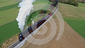 Restored steam locomotive and passenger cars traveling blowing smoke and steam following ahead of train thru farm coun