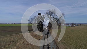 Restored steam locomotive and passenger cars traveling blowing smoke and steam following ahead of train thru farm coun