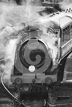 Restored Victorian era steam train engine with full steam in black and white