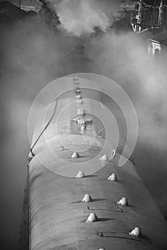 Restored Victorian era steam train engine with full steam in black and white