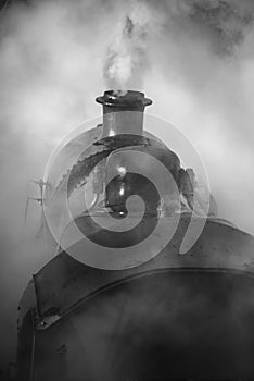 Restored Victorian era steam train engine with full steam in black and white