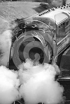 Restored Victorian era steam train engine with full steam in black and white