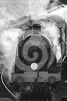 Restored Victorian era steam train engine with full steam in black and white