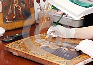 Restorer works on old gilded icon with brush