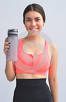 Restoring water balance. Portrait of young woman in sports wear keeping bottle in hand and smiling