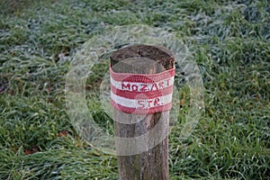 A restrictive roadside pole decorated with knitwear against a background of grass with hoarfrost in November. Berlin, Germany