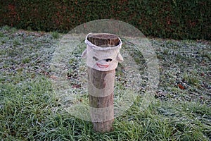 A restrictive roadside pole decorated with knitwear against a background of grass with hoarfrost in November. Berlin, Germany