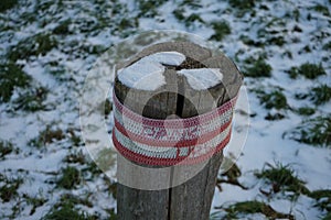 A restrictive roadside post decorated with knitwear against the background of grass under the snow in January. Berlin, Germany