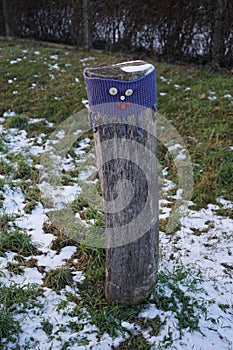 A restrictive roadside post decorated with knitwear against the background of grass under the snow in January. Berlin, Germany