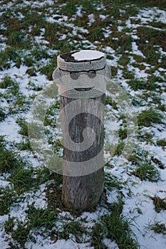 A restrictive roadside post decorated with knitwear against the background of grass under the snow in January. Berlin, Germany