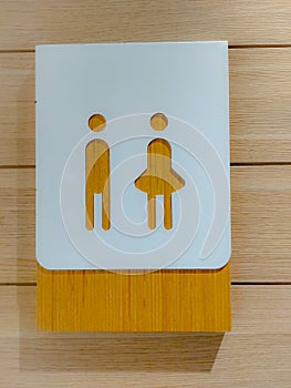 A restroom sign with pictures of woman and man on a wooden panel.