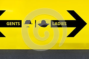 Restroom or Toilet Sign with Arrow and Hat on Yellow Wall