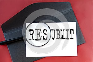 RESUBMIT - word on white paper lying on a black envelope on a red background