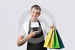 Retail store, shopping and employees concept. Friendly enthusiastic salesman, shop clerk in black apron, pointing finger