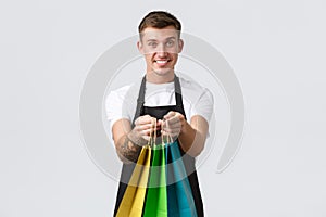 Retail store, shopping and employees concept. Friendly handsome and polite salesman handing over eco-bags with purchased