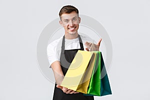 Retail store, shopping and employees concept. Friendly handsome smiling salesman, shop assistand in black apron give out