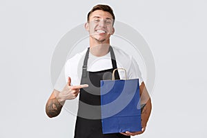 Retail store, shopping and employees concept. Handsome cheerful salesman in shop, bakery staff pointing finger at eco