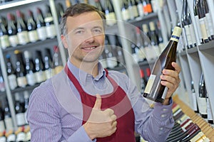 Retailer holding bottle wine and making positive gesture