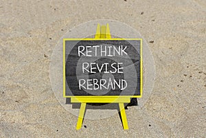 Rethink revise rebrand symbol. Concept word Rethink Revise Rebrand on beautiful blackboard. Beautiful sand beach background.