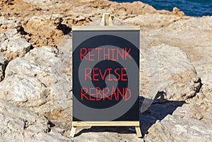 Rethink revise rebrand symbol. Concept word Rethink Revise Rebrand on blackboard. Beautiful stone beach sea blue background.