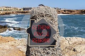 Rethink revise rebrand symbol. Concept word Rethink Revise Rebrand on blackboard. Beautiful stone beach sea blue sky background.
