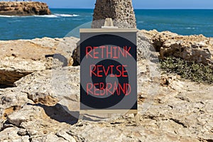 Rethink revise rebrand symbol. Concept word Rethink Revise Rebrand on blackboard. Beautiful stone beach sea blue sky background.