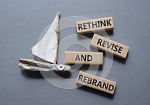 Rethink Revise and Rebrand symbol. Wooden blocks with words Rethink Revise and Rebrand. Beautiful grey background with boat.