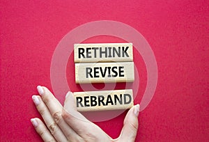 Rethink Revise Rebrand symbol. Wooden blocks with words Rethink Revise Rebrand. Beautiful red background. Businessman hand.
