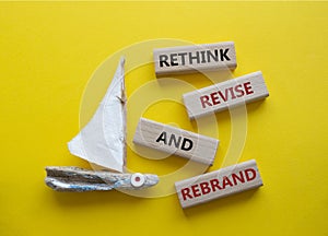 Rethink Revise and Rebrand symbol. Wooden blocks with words Rethink Revise and Rebrand. Beautiful yellow background with boat.