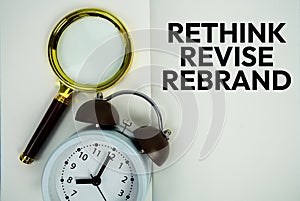 Rethink Revise Rebrand text with magnifying glass and alarm clock flat lay on notepad background photo