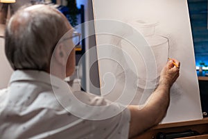 Retired artist sketching creative vase model using pencil on white canvas on wooden easel