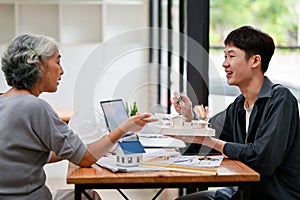A retired Asian female client discussing her home building design with an architect in the office