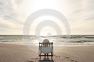 Retired biracial senior woman sitting on folding chair relaxing at beach in front of horizon on sea