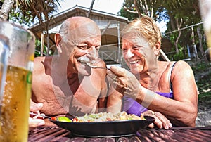 Retired couple having fun eating local food at thai restaurant beach bar outdoors - Mature man and woman on active elderly