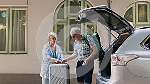 Retired couple loading voyage luggage in car trunk