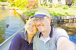 A retired couple is making selfie on the boat in Giethoorn canal Netherlands / old couple having fun in the Venice of North