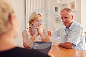 Retired Couple Meeting With Female Financial Advisor In Kitchen At Home