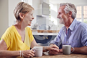 Retired Couple Sitting Around Table At Home Having Morning Coffee Together