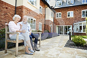 Retired Couple Sitting On Bench With Hot Drink In Assisted Living Facility